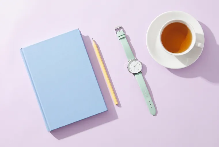 Illustration seen from above: a closed blue notebook, a yellow pencil, a wristwatch and a cup of tea on a lilac table.